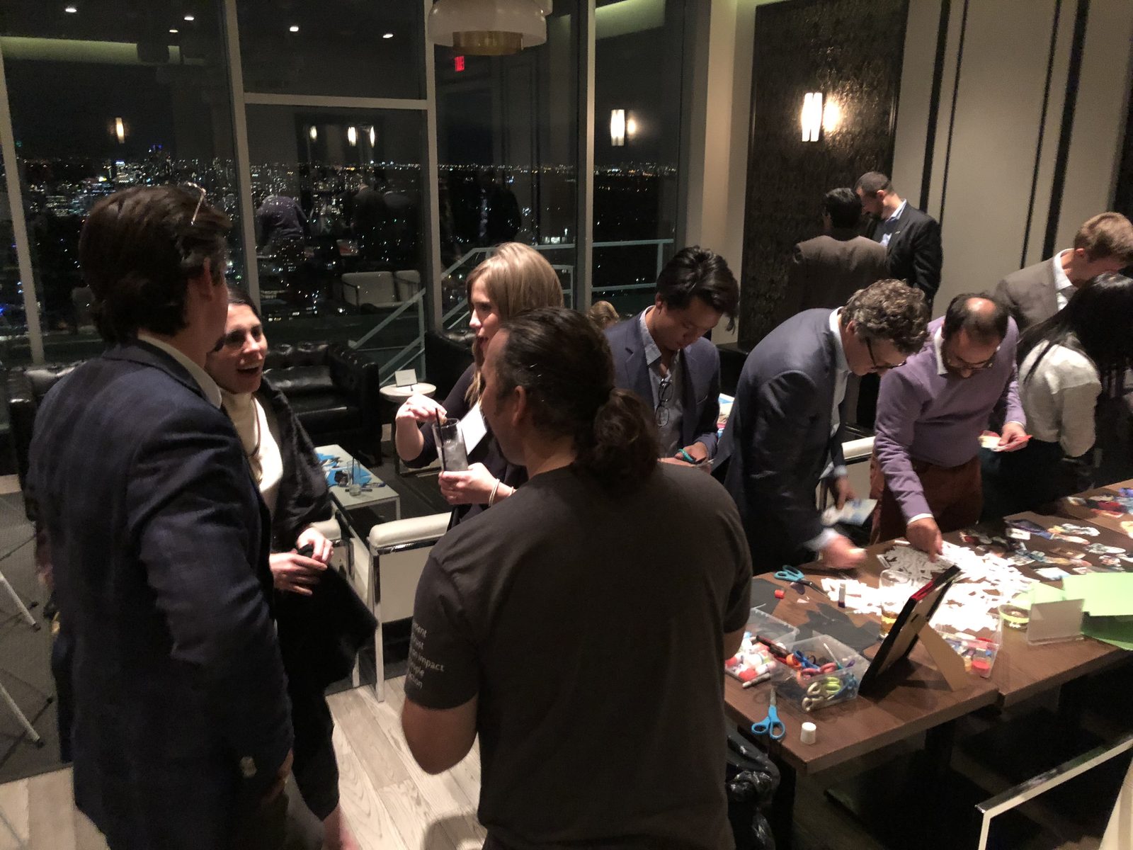 Guests in business attire gathered around a long collage table at an evening event