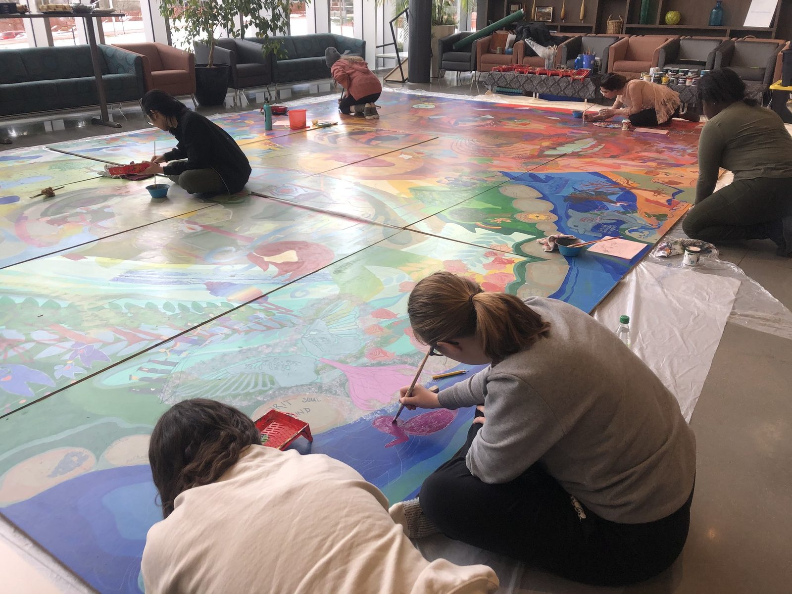 Participants painting a very large canvas laid across a floor